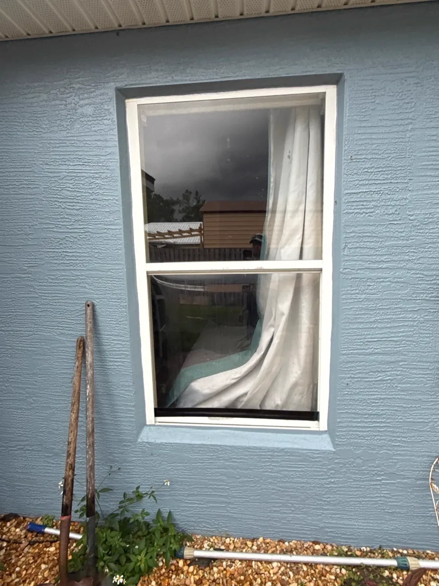 A single white-framed impact window set into a blue stucco wall, finished with a crisp perimeter seal.