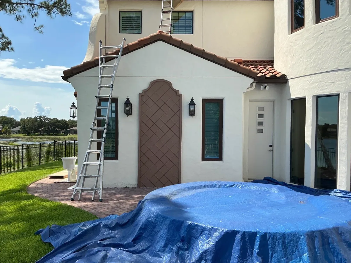 Bronze-framed impact windows and a wide glass door going into a stucco home, with the yard covered while the crew works.