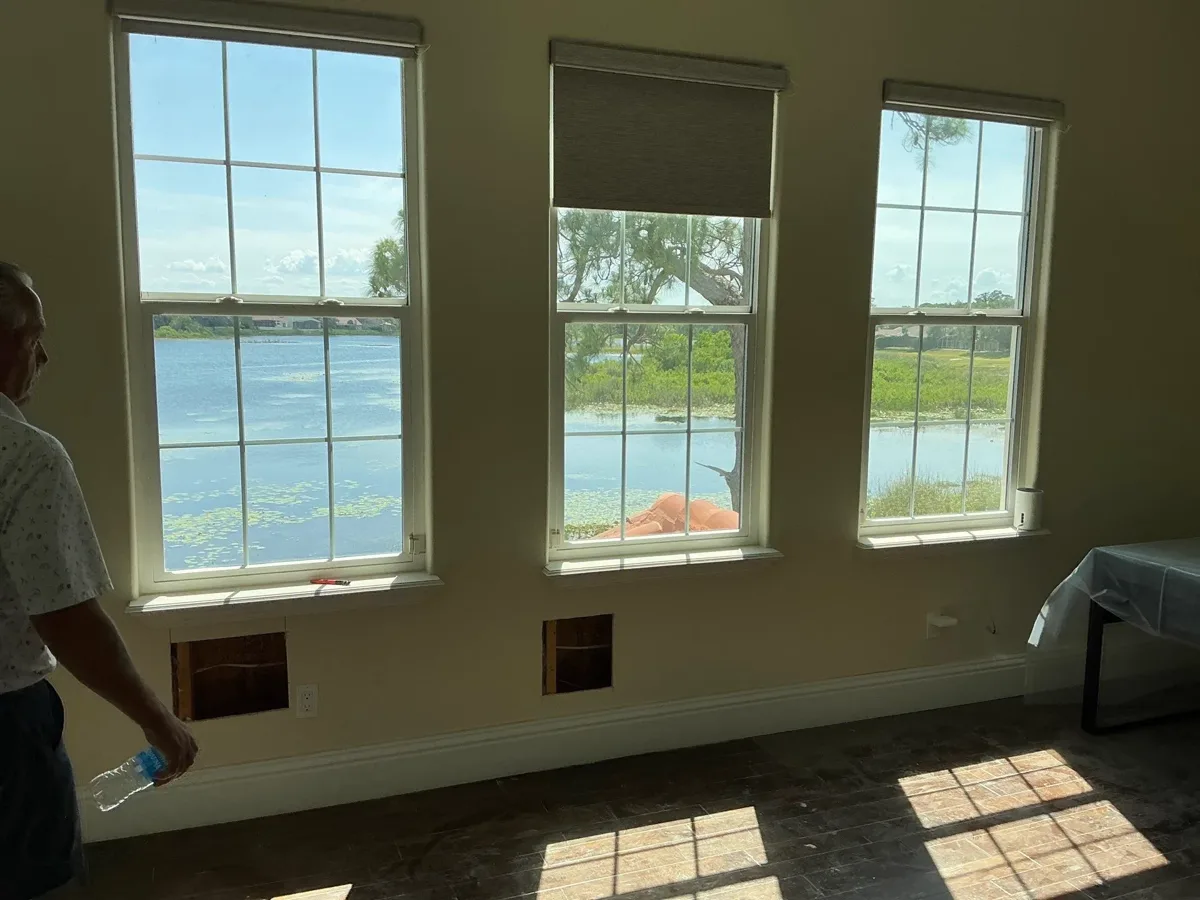 Three white double-hung windows with grids, framing a lake view from inside the living room.